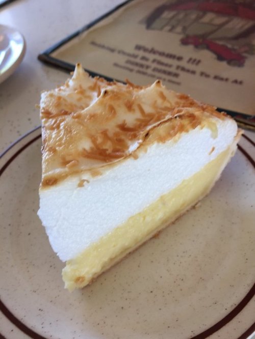 A slice of coconut cream pie with a golden toasted meringue topping on a white plate.