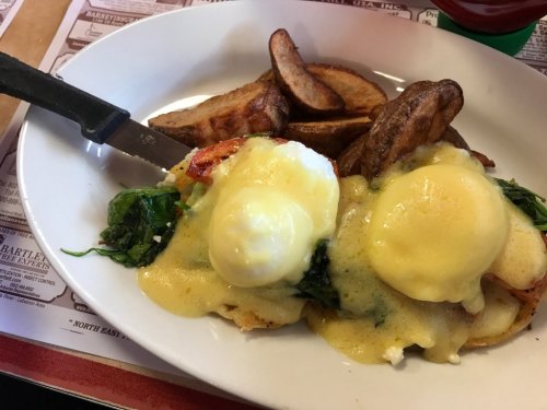 A plate of eggs Benedict with poached eggs, spinach, and hollandaise sauce, served with potato wedges.