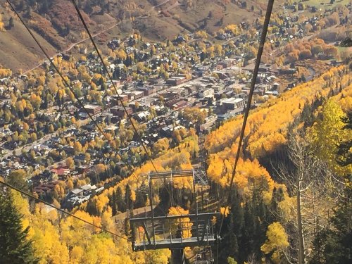 Aerial view of a town surrounded by vibrant autumn foliage and a ski lift in the foreground.