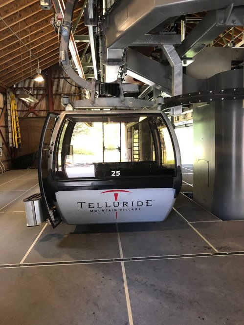 A Telluride Mountain Village gondola cabin inside a station, with a wooden ceiling and open space around it.