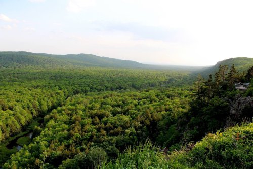 A panoramic view of a lush green valley surrounded by rolling hills under a partly cloudy sky.