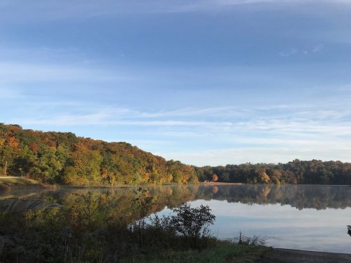A serene lake surrounded by autumn foliage, reflecting the colorful trees under a clear blue sky.