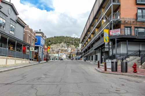 Empty street lined with buildings, shops, and a distant view of a hillside under a cloudy sky.
