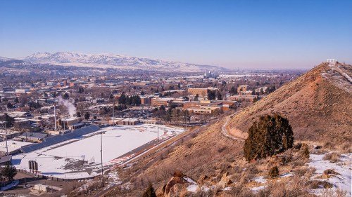 A panoramic view of a snowy town with mountains in the background, featuring a stadium and buildings below.
