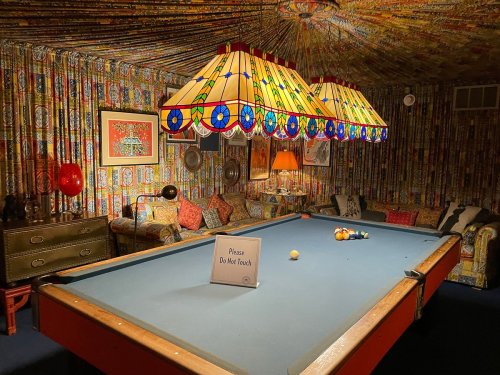 A cozy game room with a pool table, colorful patterned wallpaper, and vintage lamps hanging from a ceiling.