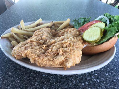A plate with fried chicken, French fries, and a sandwich with lettuce, tomato, pickles, and onions.
