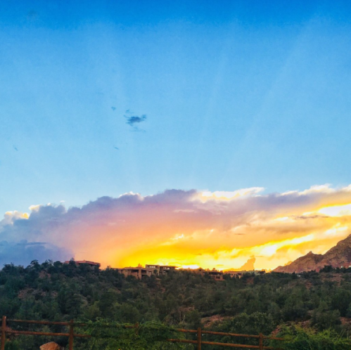 A vibrant sunset over a mountainous landscape, with colorful clouds and rays of light illuminating the sky.