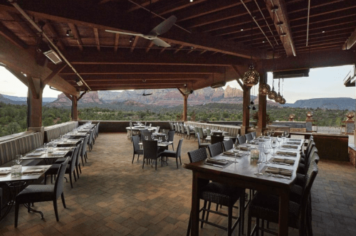 Outdoor dining area with tables set for guests, overlooking scenic mountains and greenery in a warm, inviting atmosphere.