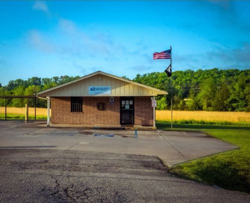 A small brick building with a postal service sign, an American flag, and a grassy area in the background.
