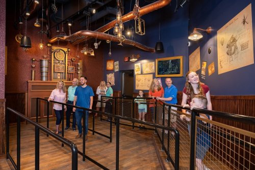 A group of people stands in a themed indoor queue, surrounded by vintage decor and wall art.