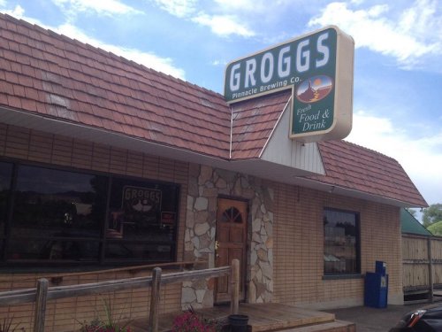 Exterior of Groggs Pinnacle Brewing Co. featuring a stone facade, wooden deck, and a sign for food and drink.