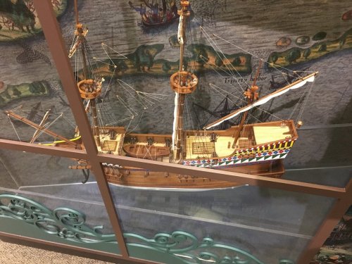 A detailed model of a historic ship displayed behind glass, set against a colorful map background.