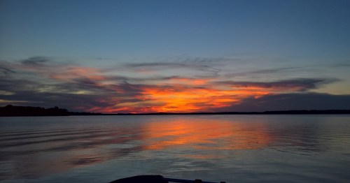 A vibrant sunset over a calm lake, with colorful clouds reflecting on the water's surface.