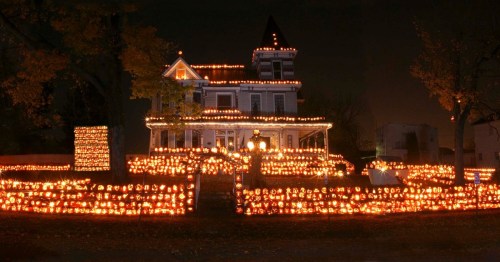 A beautifully lit house surrounded by glowing jack-o'-lanterns, creating a festive Halloween atmosphere at night.
