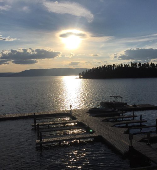 A serene lake view at sunset, with a wooden dock and distant hills silhouetted against the glowing sky.
