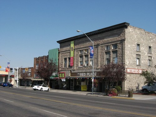 Historic buildings line a street, featuring shops and signage under a clear blue sky.