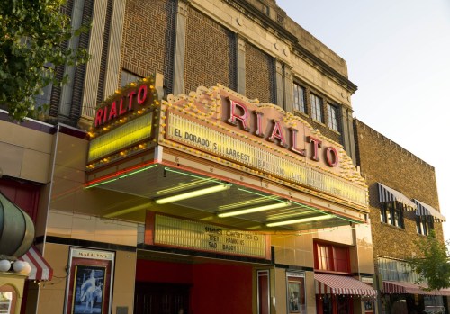 The historic Rialto theater marquee, featuring bright lights and vintage design, stands prominently in a cityscape.