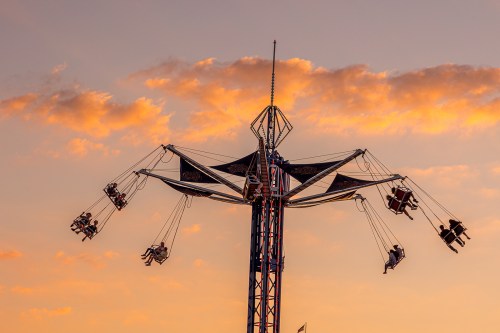 A swing ride at sunset, with riders suspended in the air against a colorful sky.