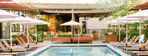 A serene pool area with lounge chairs, umbrellas, and a modern outdoor dining space surrounded by greenery.