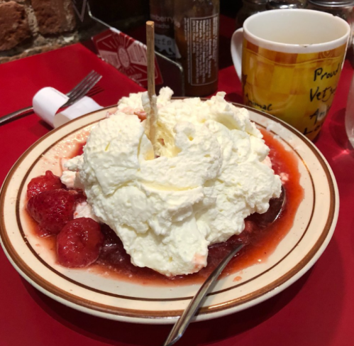 A dessert plate with whipped cream, strawberries, and a wooden stick, set on a red tablecloth.