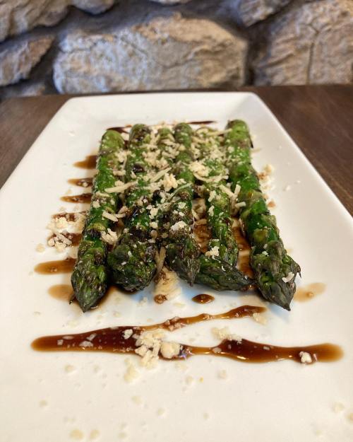 Grilled asparagus drizzled with sauce and topped with grated cheese, served on a white plate.