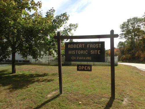 Sign for the Robert Frost Historic Site, indicating parking and that the site is open, surrounded by greenery.