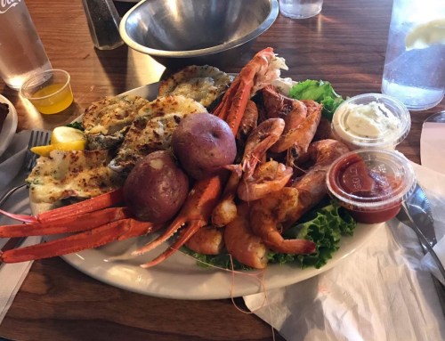 A seafood platter featuring crab legs, shrimp, potatoes, and dipping sauces on a bed of lettuce.