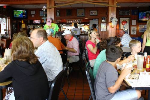 A busy restaurant scene with diners at tables, chatting and enjoying meals, surrounded by decor and a bar area.