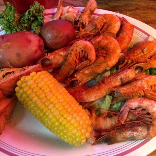 A plate of fried shrimp, boiled potatoes, corn on the cob, and lettuce, garnished with leafy greens.