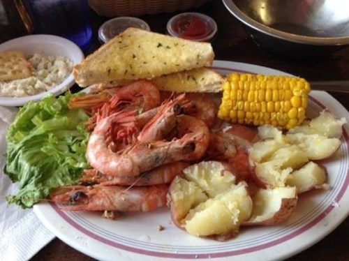 A plate of shrimp, corn on the cob, baked potatoes, garlic bread, and a side of coleslaw.