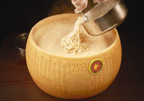 A large wheel of cheese with noodles being poured into it, creating a creamy pasta dish.