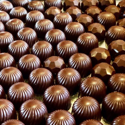 A close-up of numerous shiny chocolate confections arranged in a neat pattern.
