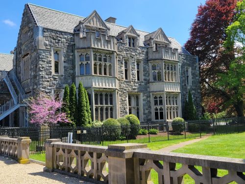 A large stone mansion with intricate architecture, surrounded by greenery and colorful trees under a clear blue sky.