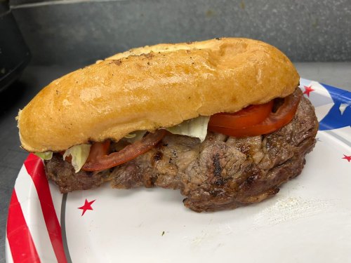 A hearty sandwich with grilled meat, lettuce, and tomato, served on a toasted bun on a patriotic-themed plate.