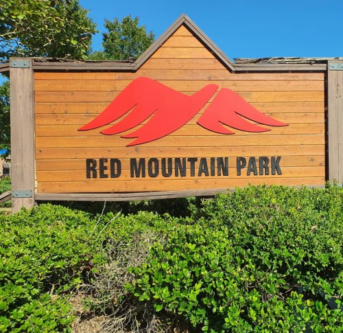 Sign for Red Mountain Park featuring red mountain graphics and surrounded by greenery.