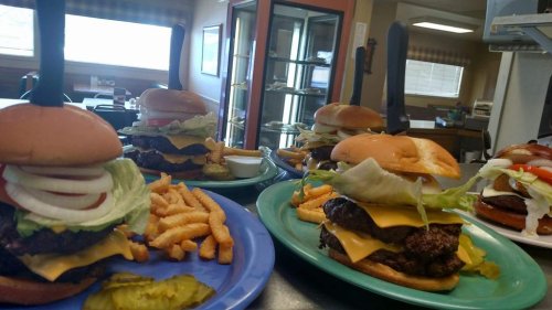A table with large burgers topped with lettuce, onions, and cheese, served with fries and pickles in a casual dining setting.