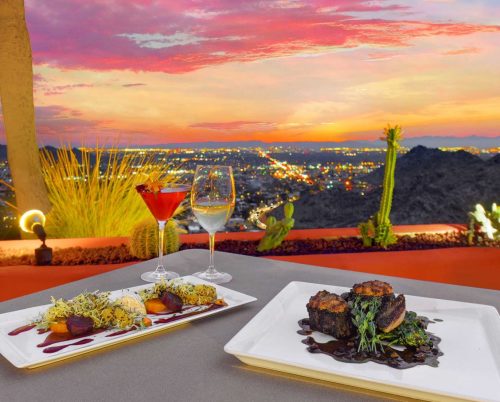 A scenic sunset view with two elegant plates of food and drinks, overlooking a city skyline.