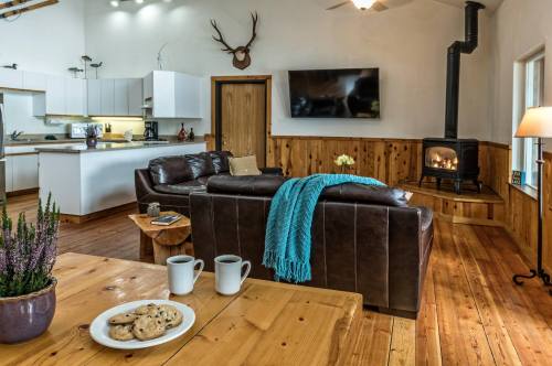 Cozy living room with a leather couch, wooden accents, a fireplace, and a table with cookies and mugs.