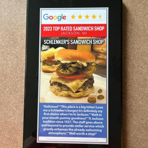 A smartphone displays a review for Schlenker's Sandwich Shop, featuring a burger with pickles and cheese.