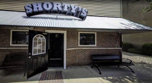 Exterior of Shorty's, featuring a brick facade, a black door, and a covered entrance with a bench.