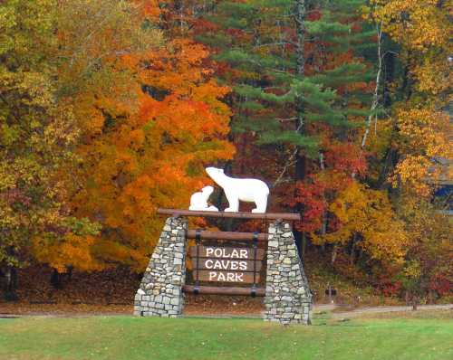 Sign for Polar Caves Park with a white bear sculpture, surrounded by vibrant autumn foliage.