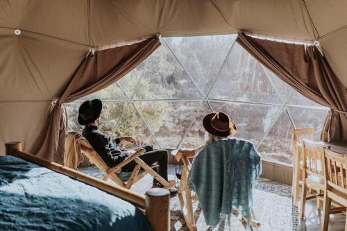 Two people relax in a geodesic dome, enjoying the view through large windows, surrounded by cozy furnishings.