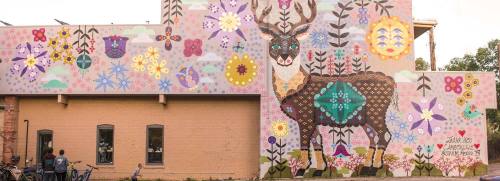 Colorful mural featuring a deer surrounded by flowers and plants on a building wall, with people and bicycles nearby.