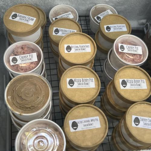 Containers of various desserts, including pies and creams, labeled and arranged in a display case.