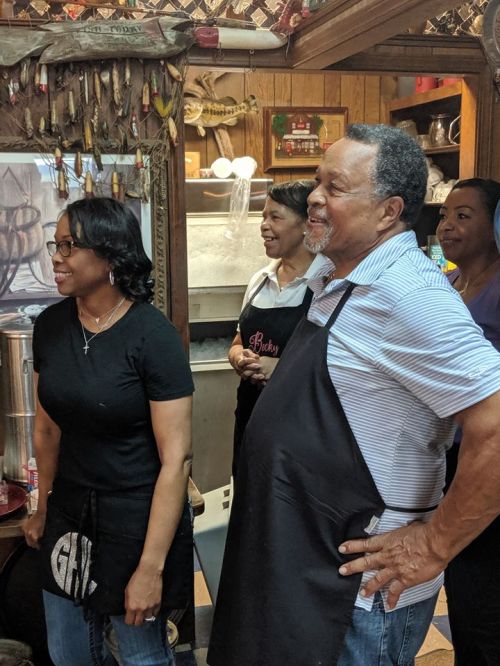 A group of four people smiling and interacting in a cozy restaurant setting, wearing aprons and enjoying each other's company.