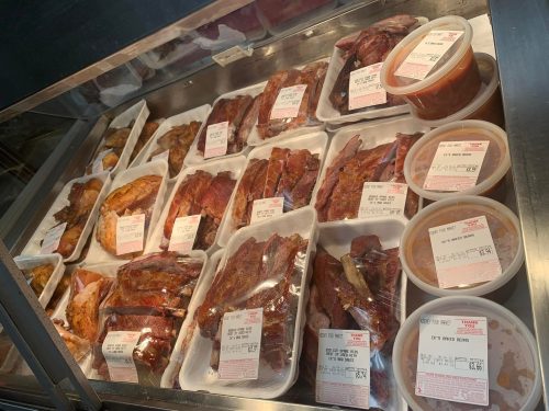 A display case filled with various packaged meats and sauces, labeled with price tags.