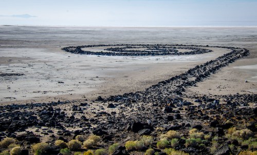 A spiral stone formation on a barren landscape, surrounded by sparse vegetation and a distant horizon.