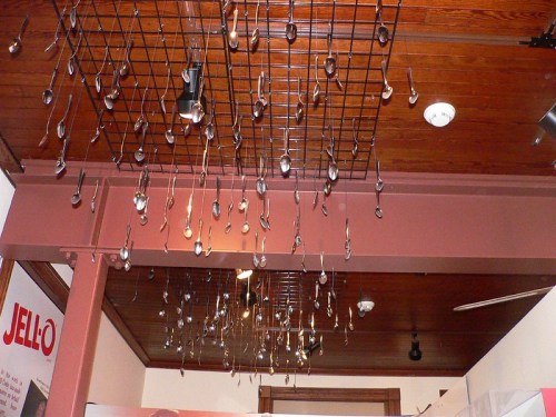 A ceiling installation featuring numerous hanging spoons against a wooden backdrop.