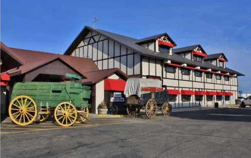 Historic wagons in front of a two-story building with a red and white facade under a clear blue sky.