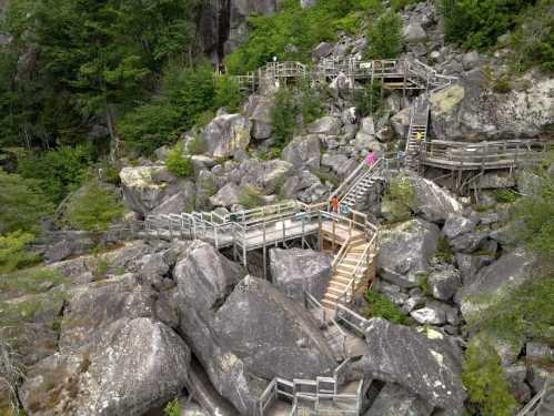 Wooden walkways and stairs wind through large boulders and greenery in a natural landscape.